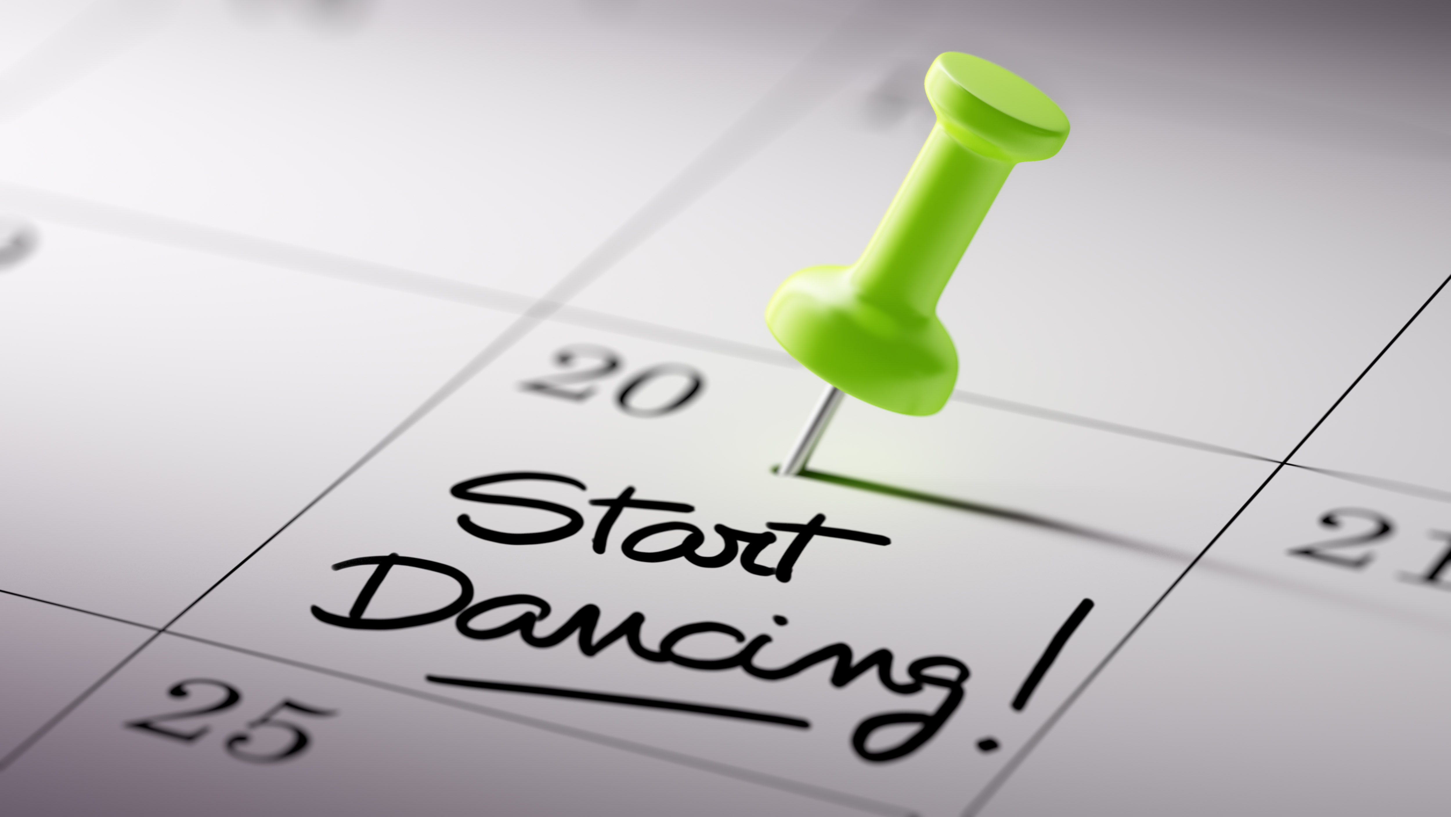 Concept image of a Calendar with a green push pin. Closeup shot of a thumbtack attached. The words Start Dancing written on a white notebook to remind you an important appointment.